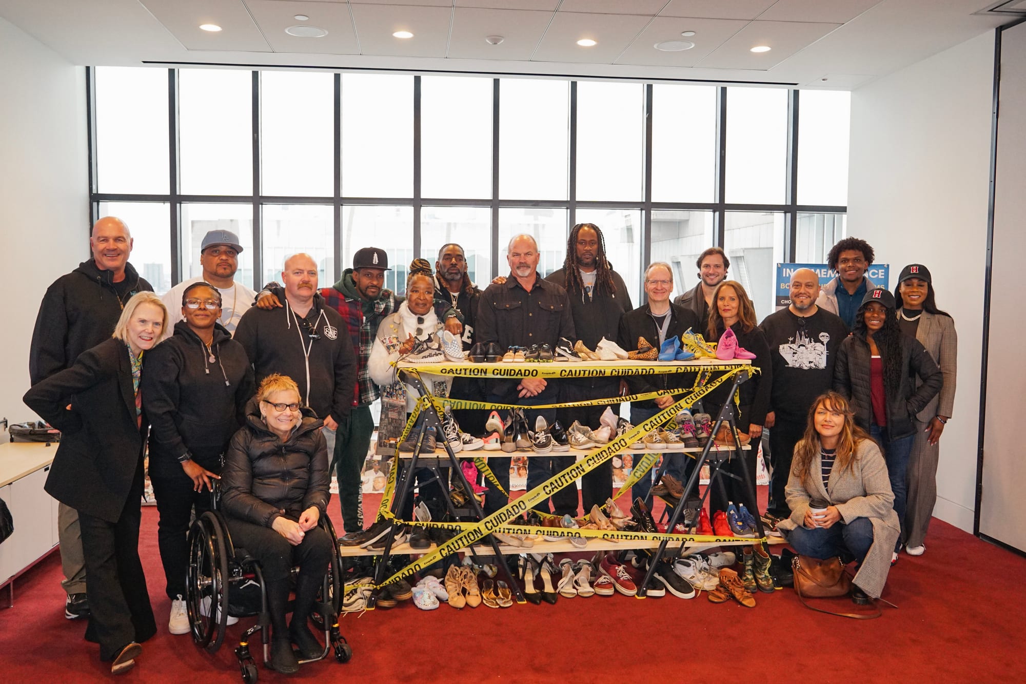 The filmmakers, producers and community of Nothing to See Here: Watts gathered behind a display of children's shoes marked with caution tape, in a daylit room