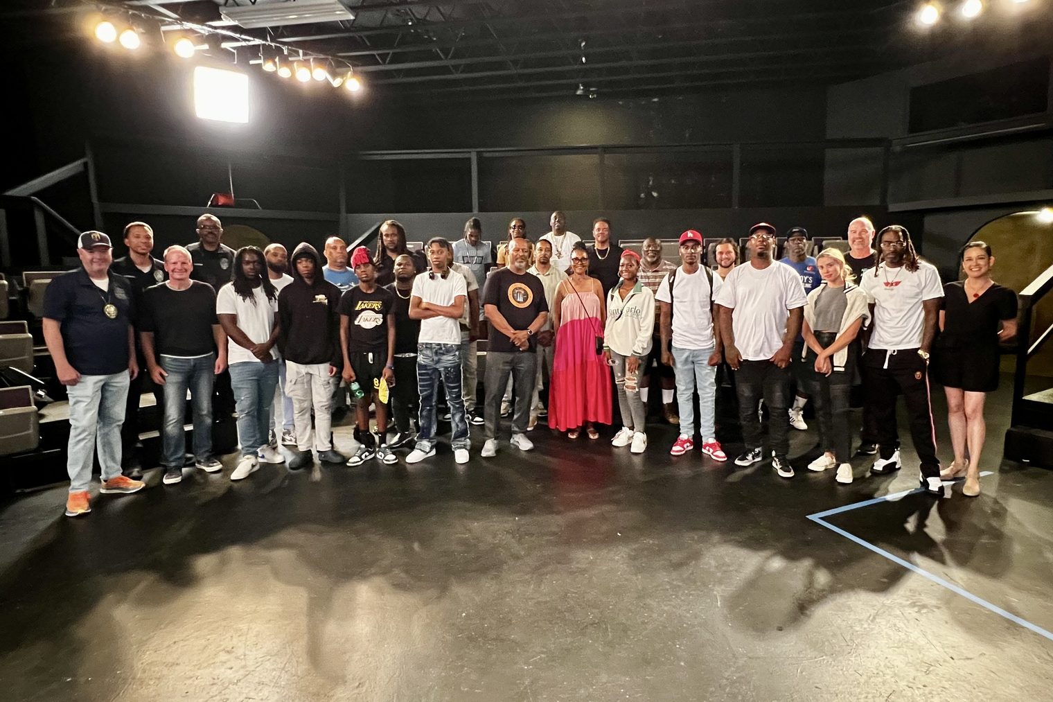 The filmmaking team of Nothing to See Here: Watts standing together in a row across a theatre floor, under the stage lights