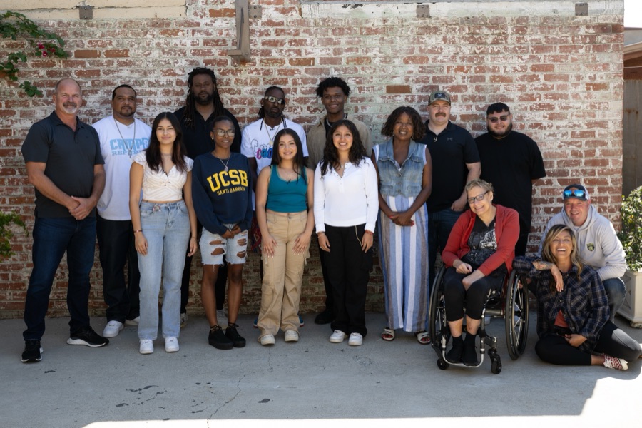 The Watts filmmakers together against a brick wall, fifteen of them, outdoors in the sun.