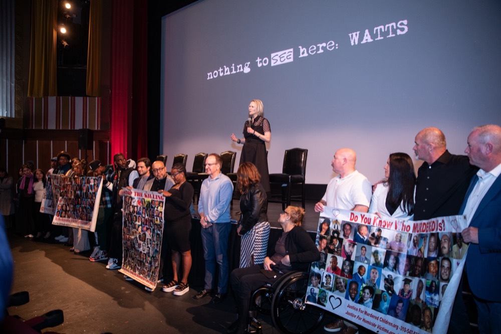 Filmmakers on stage at Coolidge Corner holding a banner of faces, the title on the screen behind them